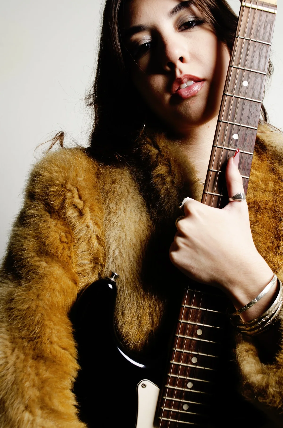 Modelo con tapado de piel sostiene una guitarra eléctrica y mira a cámara