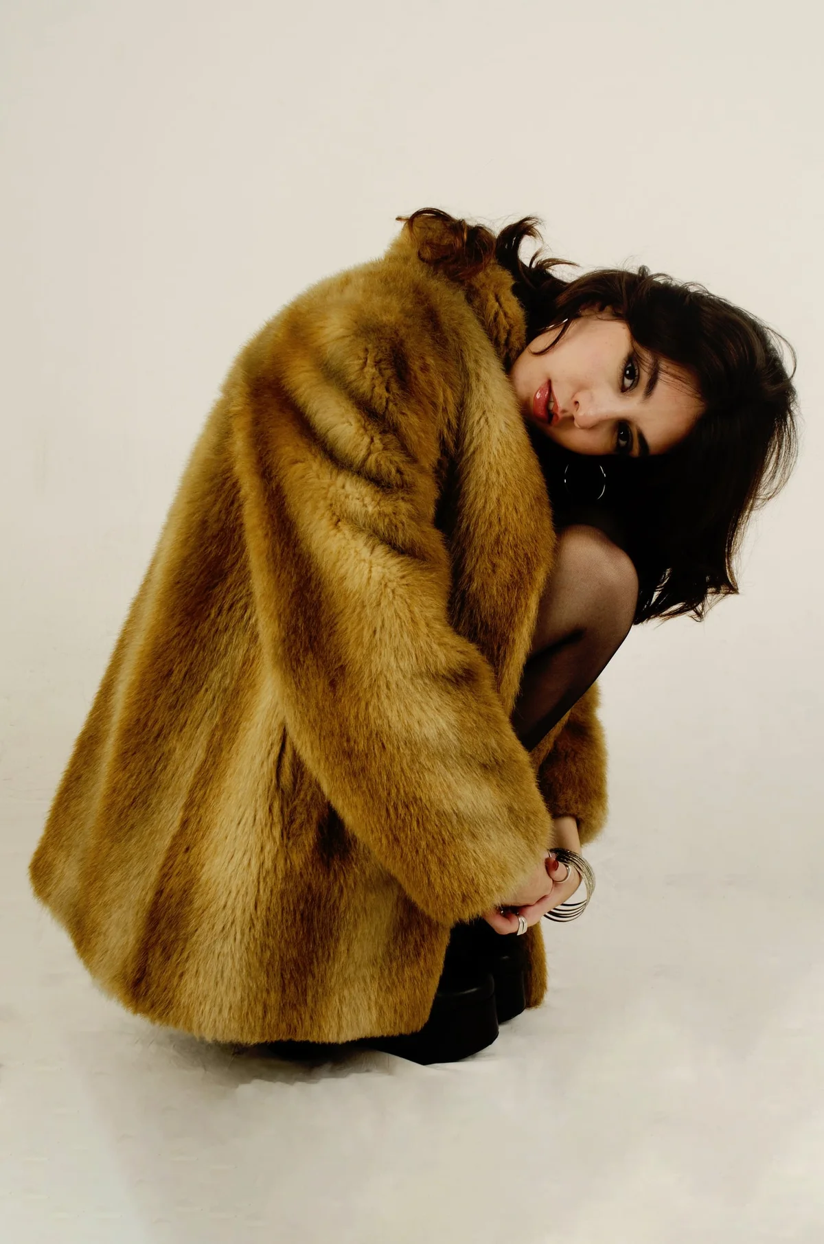 Modelo agachada con tapado de piel sobre fondo blanco