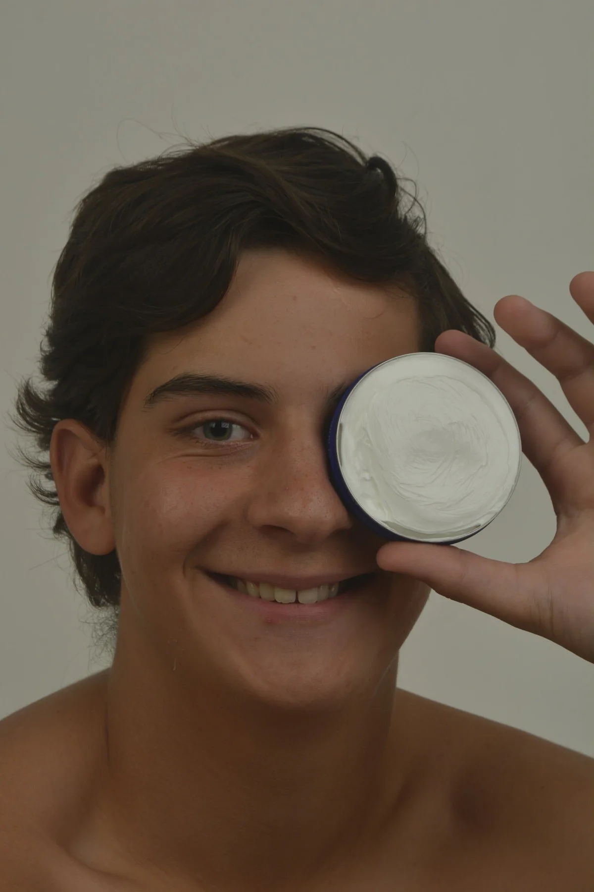 Modelo sonriente se tapa un ojo con un pote de crema abierto