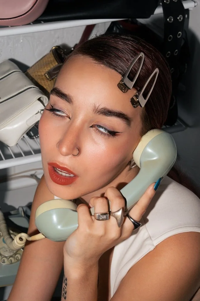 Modelo con hebillas en el pelo hablando por un teléfono antiguo verde