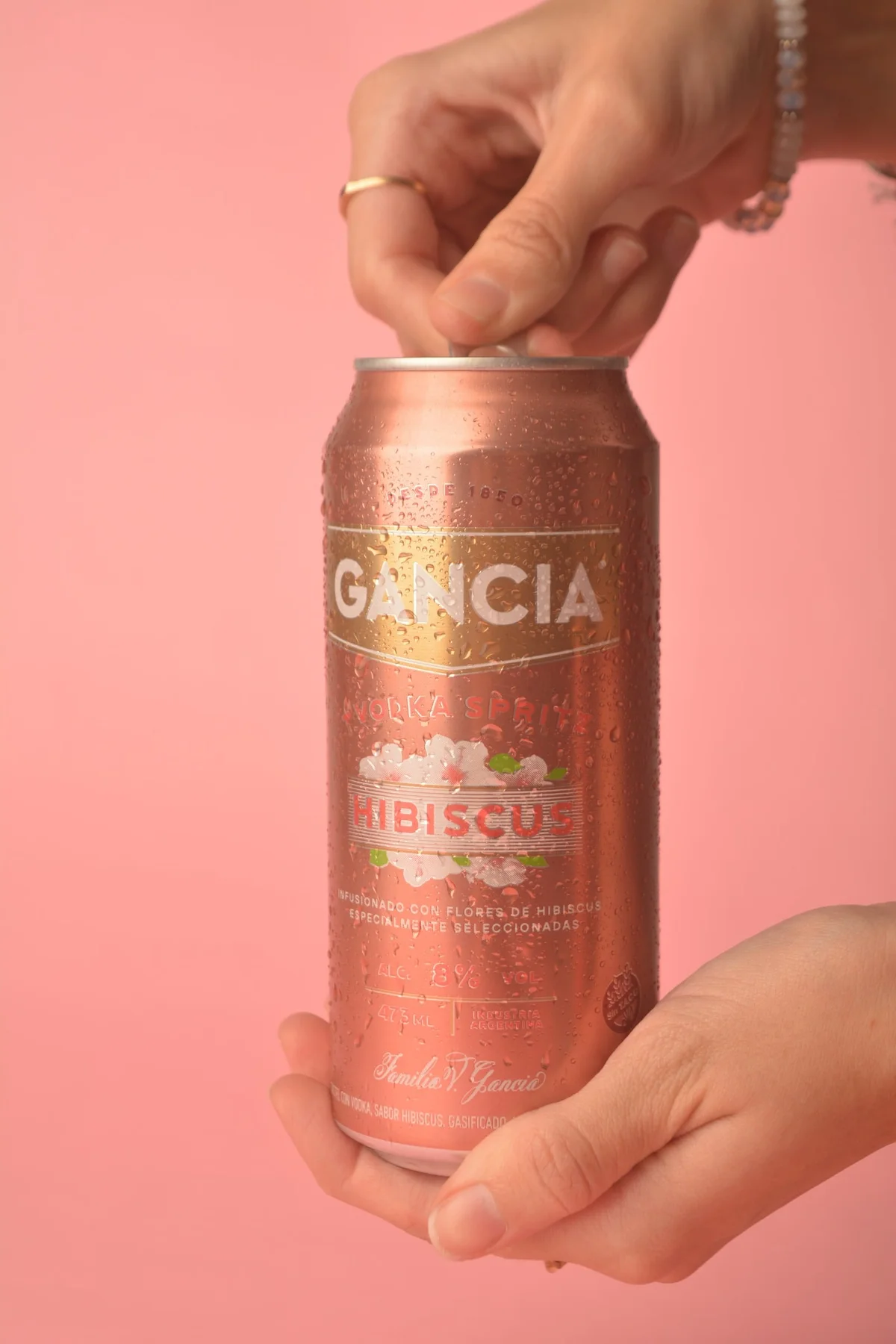 Manos abriendo una lata de Gancia Hibiscus sobre fondo rosa